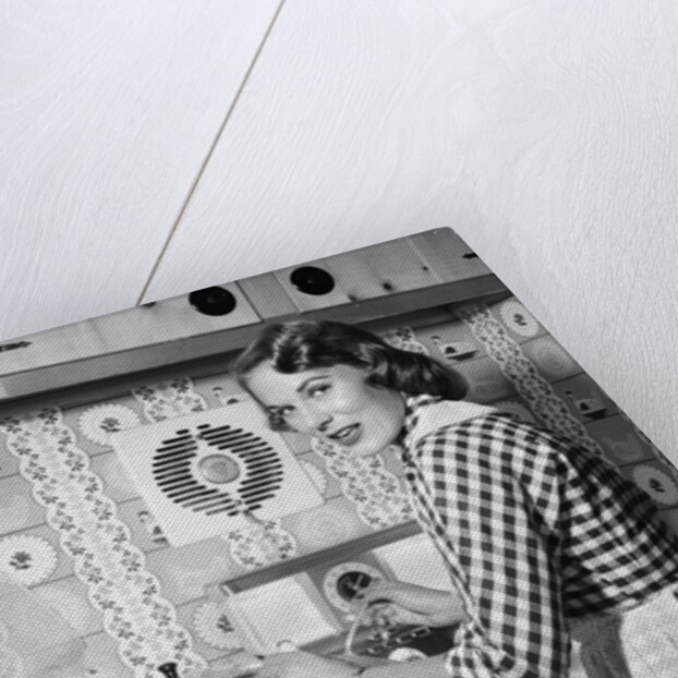 1950s Housewife Wearing Checkered Dress Standing In Kitchen Stirring Pot On Stove Looking Over Shoulder by Anonymous