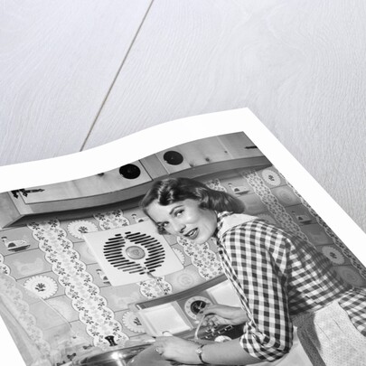 1950s Housewife Wearing Checkered Dress Standing In Kitchen Stirring Pot On Stove Looking Over Shoulder by Anonymous