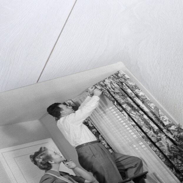 1950s Skeptical Wife In Apron Fingers Pressing Chin Watching Husband On Ladder Hanging New Jungle Motif Drapes In Living Room by Anonymous