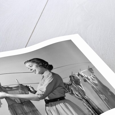 1950s Smiling Woman Housewife Hanging Wash Child Dress On Clothesline To Dry by Anonymous
