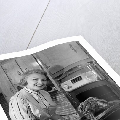 1950s Smiling Woman Housewife Wearing Apron Taking Large Roast Beef From Electric Oven In Kitchen Looking At Camera by Anonymous