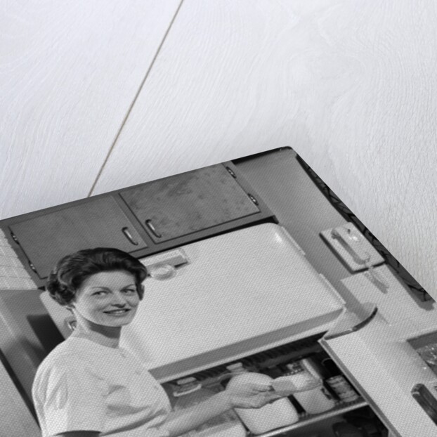1950s Smiling Woman Housewife Putting Stick Of Butter Into Electric Refrigerator In Kitchen Looking At Camera by Anonymous