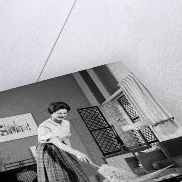 1950s 1960s Woman Wearing A White Blouse & Plaid Skirt Dusting With A Feather Duster A Glass Top Coffee Table by Anonymous