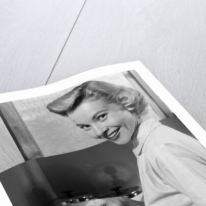 1950s Smiling Blonds Woman Mother Warming A Baby Bottle Of Milk In Kitchen Looking At Camera by Anonymous