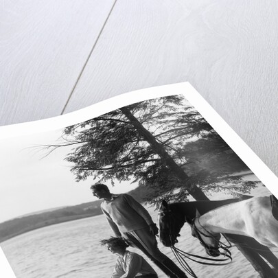 1930s Man Standing On Rock Lakeside Holding Reins Of Two Horses With Woman Seated Beside Looking Off To Side by Anonymous