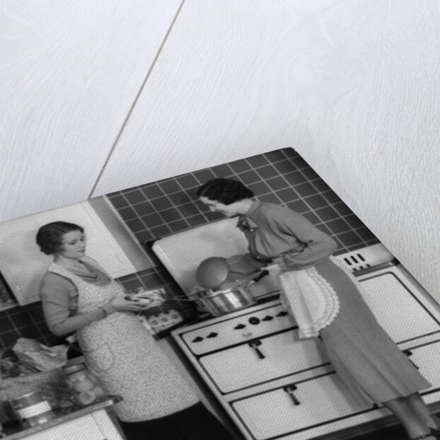 1930s Woman Housewife And Friend Wearing Apron Cooking Food In Kitchen On Gas Stove Indoor by Anonymous