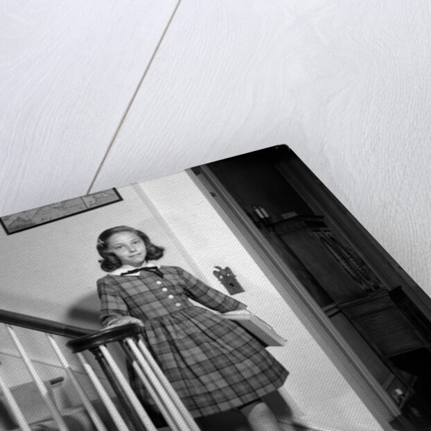 1950s Teenage Girl In Plaid Dress And White Ankle Socks On Stairway Holding Banister Carrying School Books Looking At Camera by Anonymous