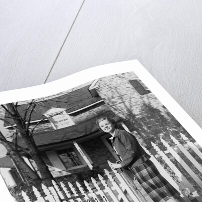 1940s Smiling Pretty Young Teenage Girl Standing By White Picket Fence In Front Of Stone House In Autumn Looking At Camera by Anonymous