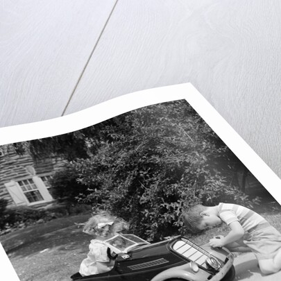 1940s 1930s Boy On Sidewalk Fixing Headlight Of Toy Car Driven By Little Girl Playing Outdoor by Anonymous
