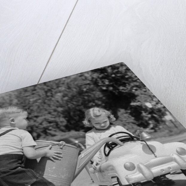 1950s Little Boy Playing Gas Station Pouring Water Into Toy Car For Little Girl by Anonymous