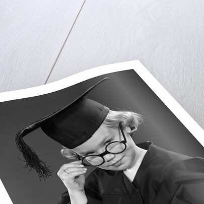 1950s Little Blond Girl Wearing Scholarly Glasses Graduation Cap And Gown Looking At Camera by Anonymous