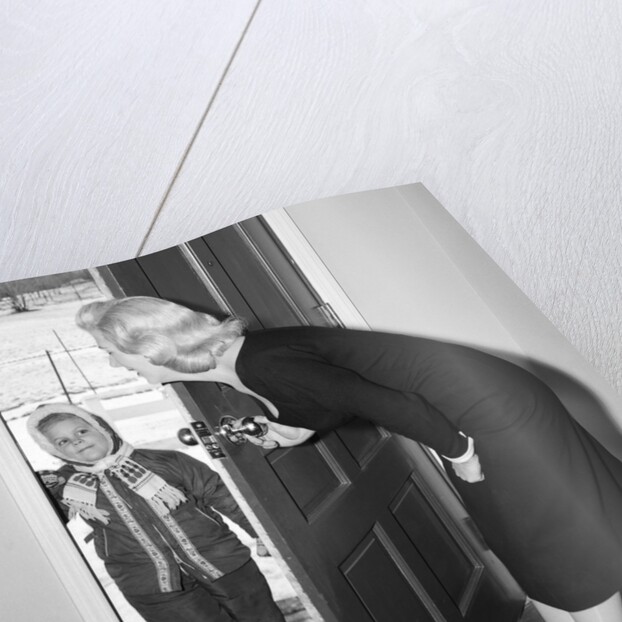 1950s Blonde Mom Opening Front Door To Let In Child Dressed Winter Snow Suit Scarf Hat Can See Snow Scene Through Door by Anonymous