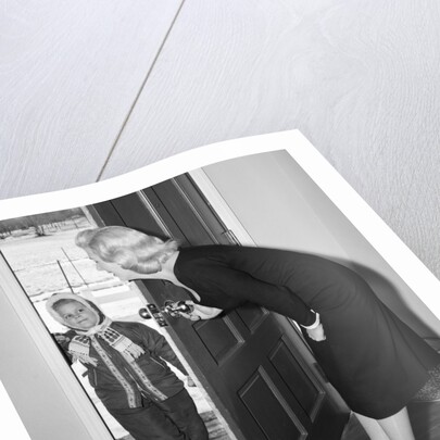 1950s Blonde Mom Opening Front Door To Let In Child Dressed Winter Snow Suit Scarf Hat Can See Snow Scene Through Door by Anonymous