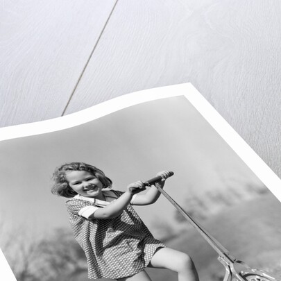 1930s Smiling Girl Playing On Scooter On Sidewalk Looking At Camera by Anonymous