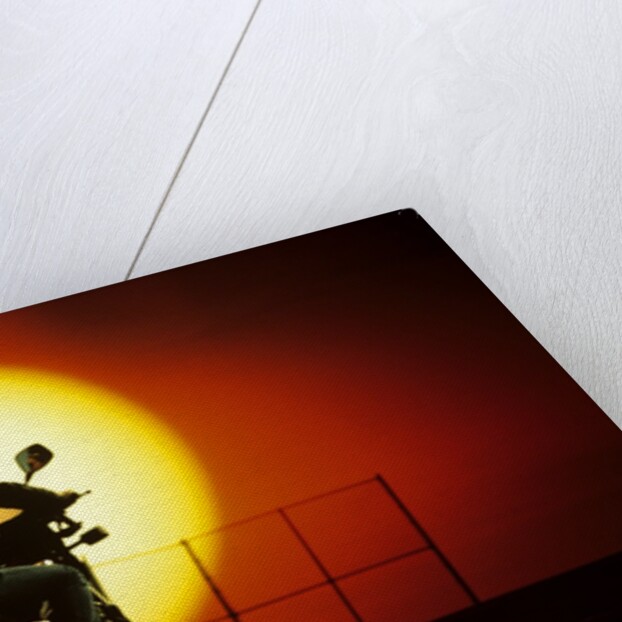 1980s silhouette of anonymous man on motorcycle driving toward rising setting sun by Anonymous