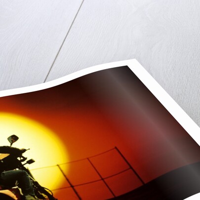 1980s silhouette of anonymous man on motorcycle driving toward rising setting sun by Anonymous