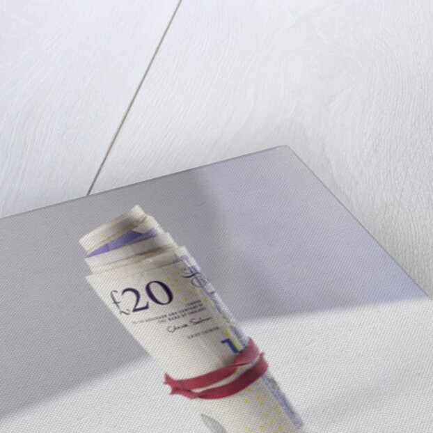 A roll of twenty pound notes on a table by Anonymous