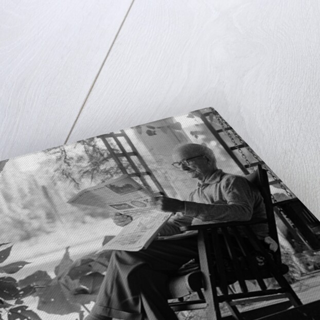 1970s elderly man reading newspaper on porch in a rocker by Anonymous