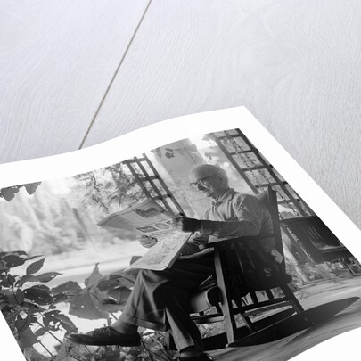 1970s elderly man reading newspaper on porch in a rocker by Anonymous