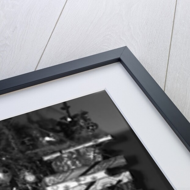 1950s portrait of young woman holding stack of presents next to a Christmas tree by Anonymous