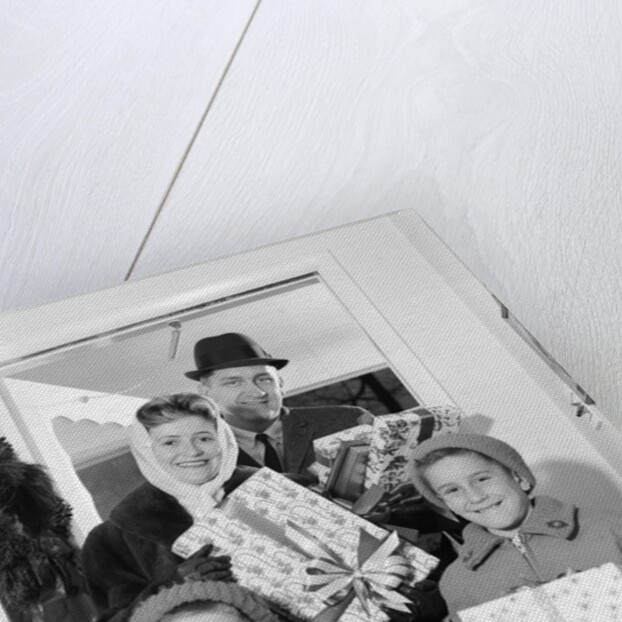 1960s family standing in doorway wearing winter coats and holding Christmas presents by Anonymous