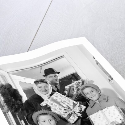 1960s family standing in doorway wearing winter coats and holding Christmas presents by Anonymous