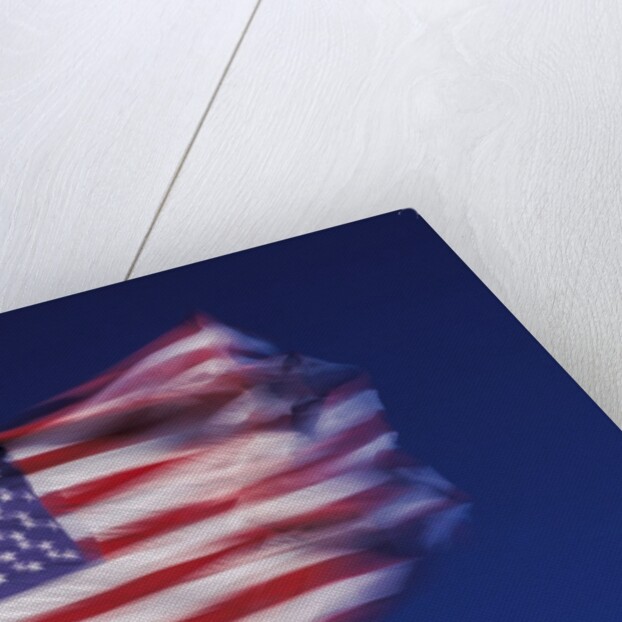 American Flag is blurred with the motion of the wind against the blue sky by Anonymous