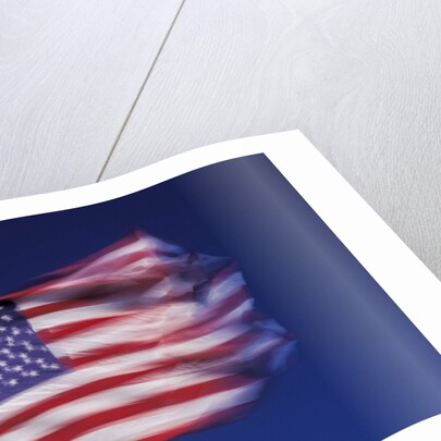 American Flag is blurred with the motion of the wind against the blue sky by Anonymous