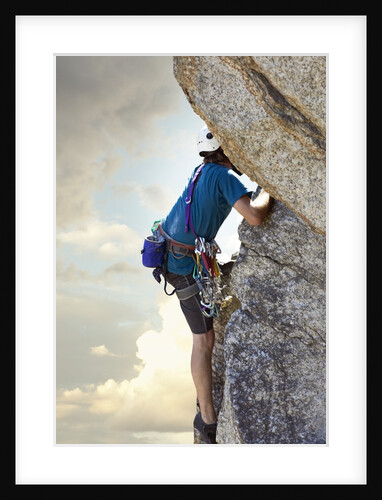 Young man rock climbing up a vertical cliff by Anonymous