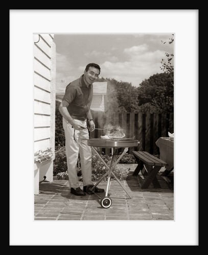 1960s Head-On View Of Man Backyard Patio Cooking Steak On Grill by Anonymous