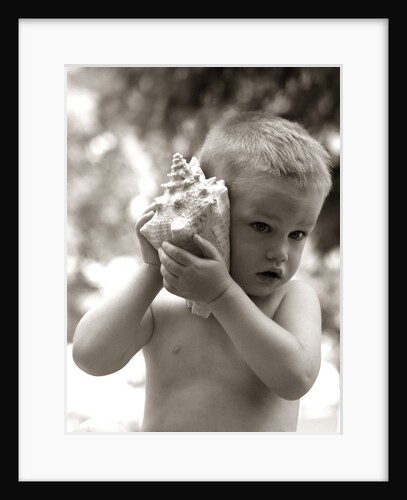 1960s Boy Toddler Holding Seashell To Ear Listening To Ocean Sounds Summer Beach by Anonymous