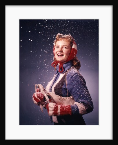 1960s Young Woman Wearing Red Mittens Ear Muffs Blue Sweater Holding Ice Skates In Falling Snow by Anonymous