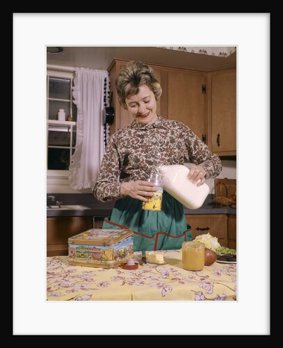 1960s Woman Housewife Mother Wearing Apron In Kitchen Pouring Milk Into Thermos For School Lunch by Anonymous