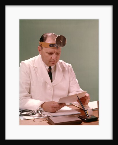 1960s Man Doctor Seated At Desk Reading Paperwork by Anonymous