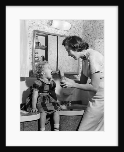 1950s Mother Feeding Medicine To Young Daughter With Mouth Wide Open Sitting On Bathroom Sink by Anonymous