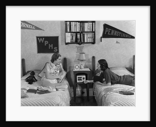 1930s 1940s Two Teen Girls Lying On Dormitory Beds Room Mates Listening To Radio College School Pennants On Wall by Anonymous
