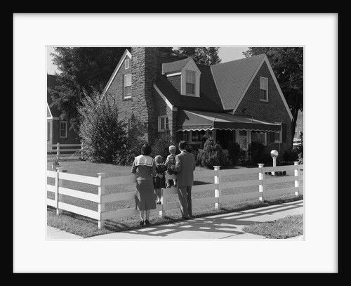 1950s Family Standing By White Fence Looking At Brick House by Anonymous