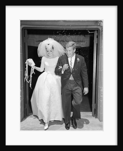 1960s Couple Bride And Groom Arm In Arm Leaving Church Under Shower Of Rice by Anonymous