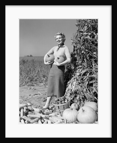 1950s 1960s Woman Standing By Corn Shock Holding A Pumpkin Under Each Arm by Anonymous