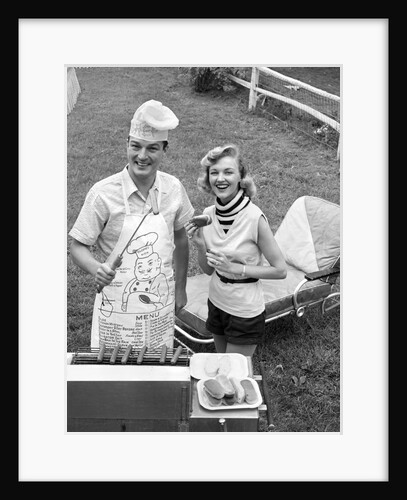 1950s Couple Backyard Grill Cook Hot Dogs Man Wearing Apron Toque and Skewered Hot Dog by Anonymous