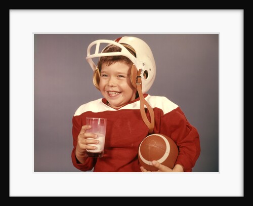 1950s 1960s Boy Drinking Milk Wearing Football Helmet Red Jersey Holding Ball by Anonymous