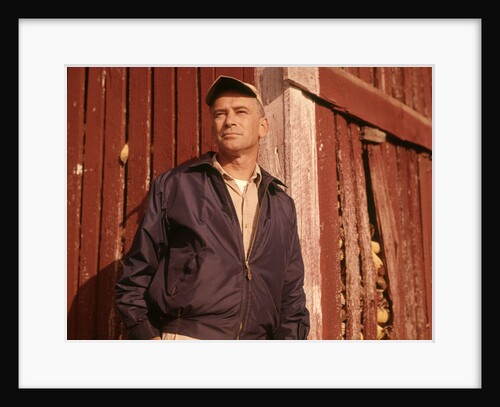 1960s Man Farmer Serious Portrait Leaning Against Corn Crib Wearing Cap And Jacket by Anonymous