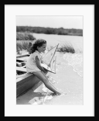 1930s Young Girl At Seashore Holding Sailboat Toy Sitting On Edge Of Rowboat Feet In Water by Anonymous