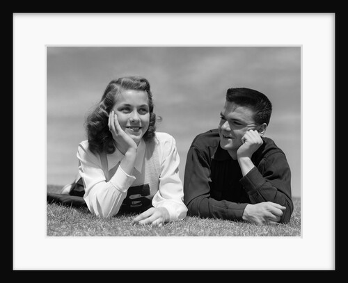 1950s Teenage Couple Laying On Grass, Boy Gazing At Girl Wearing Cheerleader Sweater by Anonymous