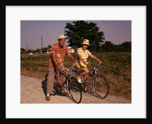 1970s Senior Elderly Retired Couple Riding Bikes Wearing Straw Hats Hawaiian Print Shirts by Anonymous