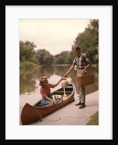 1960s Young Couple Loading Picnic Basket Thermos Into Canoe by Anonymous