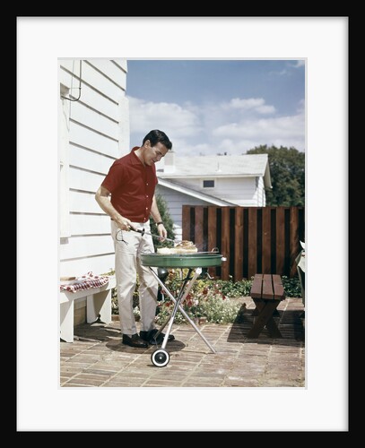 1960s Man Wearing Red Shirt Grilling Steak On Backyard Brick Patio by Anonymous