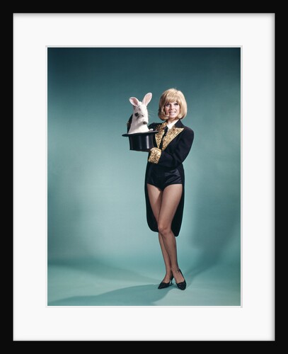 1960s Young Woman In Stage Magician Coat And Short Shorts Pulling Rabbit Out Of Top Hat by Anonymous