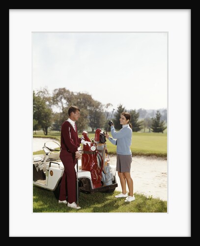 1960s Couple Man Woman Selecting Golf Clubs From Golf Bag On Cart By Sand Trap by Anonymous