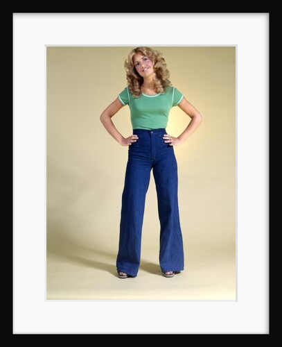 1970s Young Woman With Long Curly Hair Standing Hands On Hips In Bell Bottom Denim Blue Jeans by Anonymous